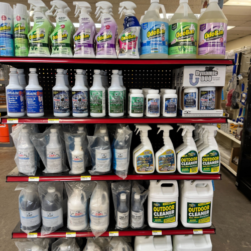 Four shelves in a store display various cleaning products, including sprays and bottles. Labels feature vivid colors and keywords like 