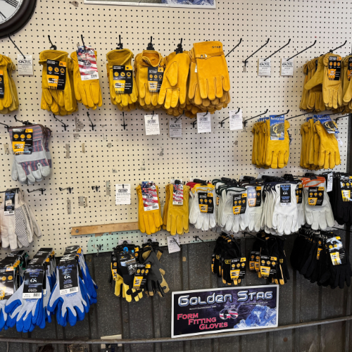 Various types of gloves, mainly yellow, white, and black, hang neatly on a pegboard display. A 