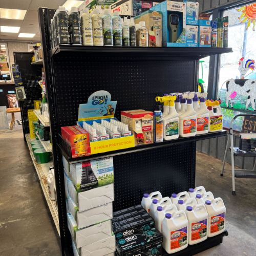 Store aisle with black shelves displaying various pest control and lawn care products, including sprays and bottles. Bright and organized setting.