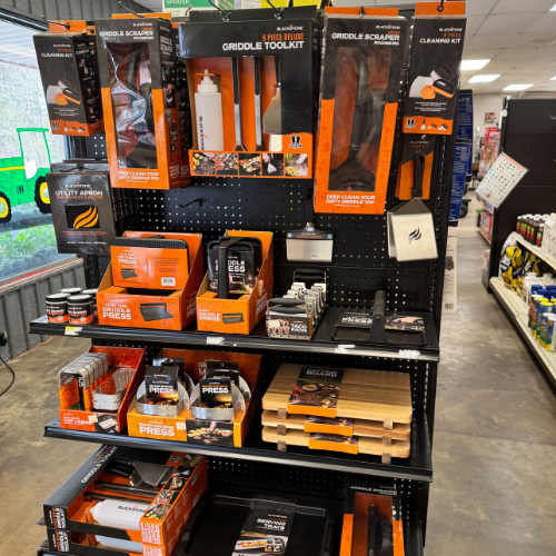 Store display of griddle accessories including tools, cleaning kits, and aprons, all in black and orange packaging. The tone is practical and inviting.