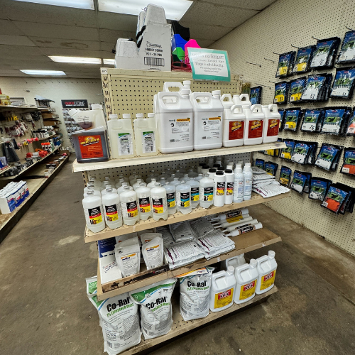 Store aisle with shelves displaying various garden and pest control products. Bottles and bags of insecticides and fertilizers are neatly arranged.