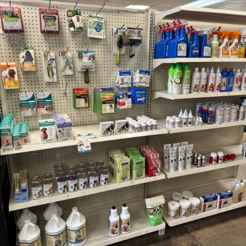 A store shelf displays various pet care products, including flea treatments, shampoos, sprays, and supplements. The shelves are neatly organized with bright packaging, conveying a sense of variety and cleanliness.